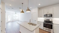 Located at 2110 Birkhall St in Raleigh, NC, this well-appointed 1-bedroom, 1-bathroom residence offers a clean, modern aesthetic throughout its efficiently organized single-floor layout. The open-concept living, dining, and kitchen area serves as the heart of the home, featuring warm hardwood-style flooring and an abundance of natural light. The kitchen is a standout, showcasing a central granite-topped island with a dual stainless steel sink, complemented by elegant brass pendant lighting overhead. White shaker-style cabinetry, subway tile backsplash, and a full suite of stainless steel appliances — including a refrigerator with ice maker, range, microwave, and dishwasher — complete this functional and stylish culinary space. A pantry provides additional storage convenience. The living area is finished with a ceiling fan and connects seamlessly to a private balcony. The spacious bedroom features plush carpeting, a ceiling fan, and a bright window, and is accompanied by a generously sized walk-in closet with built-in shelving. The bathroom offers a granite vanity, hardwood-style flooring, and a glass-enclosed walk-in shower with white subway tile surround. A utility room and additional closets throughout round out this practical and polished residence.