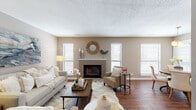 This single-story residence offers a thoughtfully designed layout with a seamless flow between living spaces. The living room serves as the focal point of the home, anchored by a brick fireplace flanked by windows with white blinds that allow ample natural light. Hardwood flooring extends through the main living areas, complementing the warm, neutral color palette found throughout the home.

Adjacent to the living room, the dining area features hardwood floors, a pendant light fixture, and large windows that brighten the space. It opens conveniently toward the bedrooms, enhancing the home's connectivity.

The galley-style kitchen is well-equipped, featuring rich dark wood cabinetry, light countertops, a subway tile backsplash, a stainless steel sink, and black appliances. A pantry closet provides additional storage.

The two bedrooms are carpeted and finished in soft neutral tones, each equipped with a ceiling fan and natural light from windows. The primary bedroom is generously sized, while the secondary bedroom offers a comfortable, well-proportioned space.

The bathrooms include dark wood vanities with light countertops and framed mirrors. One bathroom features a full tub-shower combination with clean white surrounds and wood-look flooring, maintaining the home's cohesive, warm aesthetic throughout.