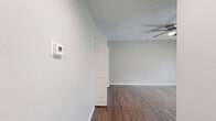 Located in Carrollton, TX (75006), this single-floor, one-bedroom, one-bathroom unit offers a well-organized and functional layout. Dark hardwood-style flooring runs throughout the living areas and bedroom, providing a cohesive and polished aesthetic. The living area is open and airy, enhanced by a ceiling fan with light fixture and neutral gray walls that reflect natural light streaming in through a sliding glass door with vertical blinds. The bedroom is a cozy, private space featuring its own ceiling fan, a window with outdoor views of lush greenery, and direct access to a closet. The galley-style kitchen is efficiently designed with gray shaker-style cabinets lining both walls, white quartz countertops, a stainless steel undermount sink, subway tile backsplash, and white appliances including an electric range and refrigerator. Warm wood flooring and a flush-mount ceiling light complete the kitchen's clean, updated look. The bathroom includes a full-sized soaking tub with an overhead shower, chrome fixtures, and white tile surround, alongside a standard toilet. A dedicated closet provides additional storage. This unit delivers practical, comfortable living in a compact and well-appointed space.