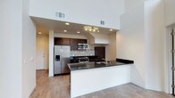 This contemporary two-floor space makes an immediate impression with its dramatic double-height ceilings in the main living area, creating an expansive, airy atmosphere that is both stylish and inviting. The open-concept layout connects the living area seamlessly to the kitchen, promoting an effortless flow throughout the space.

The kitchen is a standout feature, outfitted with rich dark espresso cabinetry that contrasts beautifully against the textured mosaic tile backsplash. Dark granite countertops extend across the full workspace and wrap around a peninsula that doubles as a breakfast bar, providing additional prep space and casual seating. A full suite of stainless steel appliances — including a French door refrigerator with water dispenser, a built-in microwave, and a gas range — ensures modern functionality. Recessed lighting and a dedicated track light fixture illuminate the cooking area with precision.

Light wood-toned flooring runs throughout the main level, lending warmth and continuity to the space. Crisp white walls amplify the natural and artificial light, keeping the interiors feeling bright and open. The two-floor layout offers distinct zones for living and privacy, making this a well-designed and highly functional space suited for a variety of lifestyles.