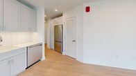 This thoughtfully designed one-bedroom, one-bathroom residence at 8605 Cameron Street in Silver Spring, Maryland offers a clean, modern aesthetic throughout. Light hardwood-style flooring runs continuously across the space, complemented by crisp white walls and recessed lighting that create a bright, airy atmosphere from entry to living area.

The welcoming entrance hallway leads past multiple closets, providing generous storage rarely found in comparably sized residences. The kitchen is a standout feature, showcasing gray shaker-style cabinetry extending to the ceiling, sleek white quartz countertops, and a striking herringbone-pattern tile backsplash. Stainless steel appliances — including a French door refrigerator, range, over-the-range microwave, and dishwasher — complete the well-appointed cooking space. A dedicated laundry area adds everyday convenience.

The open-concept layout seamlessly connects the kitchen to the dining and living areas, creating an efficient yet comfortable space for both relaxing and entertaining. The bedroom is a serene retreat, distinguished by expansive floor-to-ceiling windows that flood the room with natural light and frame elevated views of the surrounding Silver Spring cityscape and treetops.

The bathroom is finished with equal care, featuring a herringbone-patterned tile floor in warm tones, full subway tile surround in the tub/shower combo, a white vanity with under-mount sink, and a modern mirror — all combining clean lines with timeless style.