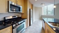 This single-floor residence is designed with an open-concept layout that promotes a seamless flow between the main living areas. Rich hardwood flooring extends throughout the hallway, living room, and kitchen, creating a warm and cohesive aesthetic. The spacious living area is anchored by floor-to-ceiling sliding glass doors that open onto a private balcony, flooding the interior with natural light and providing views of the surrounding urban landscape.

The kitchen is thoughtfully designed with light maple cabinetry reaching toward the ceiling for ample storage, dark granite countertops, and a full suite of stainless steel appliances including a gas range, over-the-range microwave, refrigerator, and dishwasher. Pendant lighting and recessed track lighting illuminate the space effectively. A kitchen island with additional counter space adds functionality and defines the boundary between the kitchen and living area. An in-unit washer and dryer are conveniently tucked nearby.

The bedroom features plush carpeting, a window with natural light, and access to a generously sized walk-in closet equipped with wire shelving. The bathroom includes a soaking tub with dark tile surround, a floating wood vanity, and tile flooring, completing this well-appointed residence.