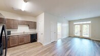 Located at 400 Katrina Court in Midlothian, Virginia, this well-appointed 2-bedroom, 2-bathroom residence offers a thoughtfully designed single-level layout. The open-concept kitchen and living area serves as the heart of the home, featuring light wood-look LVP flooring that extends throughout the main living spaces. The kitchen is equipped with rich dark-toned cabinetry, granite-style countertops, and black Whirlpool appliances including a range, refrigerator, and dishwasher, providing ample storage and functionality. The living area flows naturally from the kitchen and is brightened by large windows and a glass door that invite generous natural light. Both bedrooms are finished with plush carpet flooring and feature bright, neutral walls. The primary bedroom is notably spacious, benefiting from dual corner windows with outdoor views of the surrounding landscape and neighboring community. A dedicated walk-in closet with wire shelving provides excellent storage. The primary bathroom includes a soaking tub and shower combination, a granite-top vanity with dark wood cabinetry, and wood-look flooring. The overall aesthetic is clean and modern, with a neutral color palette, white trim, and a bright, airy ambiance throughout.