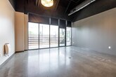Located at 5472 Wild Rose Ln in West Des Moines, Iowa, this single-floor unit delivers a striking industrial-modern aesthetic throughout its thoughtfully designed layout. The open main living area commands attention with soaring exposed ceilings that reveal structural beams and mechanical ductwork painted in a dark finish, creating a bold urban loft character. Polished concrete floors run seamlessly throughout, reflecting the abundant natural light that pours in through a dramatic floor-to-ceiling glass wall and sliding door system, which opens directly onto an outdoor patio space with string lighting and horizontal wood fencing.

The kitchen is fully equipped along one wall, featuring stainless steel appliances — including a refrigerator, range, microwave, and dishwasher — complemented by rich dark wood cabinetry, light countertops, and a single-basin sink. Pendant and linear lighting fixtures illuminate both the kitchen and living areas with warm, layered light.

A sleek hallway connects the main space to the bathroom, lined with pendant lighting and a glass-paneled sliding door that maintains the modern design language. The bathroom is finished with polished concrete flooring, a tub/shower combination, a dark wood vanity with a white countertop, and clean white walls, offering a functional and cohesive finish to this contemporary space.