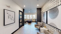 Located at 185 Polaris Point Loop in Colorado Springs, Colorado, this single-floor community lounge is thoughtfully designed to offer both comfort and functionality. The space blends contemporary aesthetics with practical amenities, making it an ideal gathering and productivity hub.

Upon entry, light-toned tile flooring and recessed lighting set a welcoming tone throughout. A bold patterned accent wall with a geometric design serves as a striking focal point, complemented by curated artwork and dark architectural column details that add visual contrast against the white walls.

The main lounge area features a plush sectional sofa, accent chairs, and a coffee table arranged around a wall-mounted flat-screen television—perfect for casual gatherings or entertainment. Natural light streams in through multiple windows that frame views of the surrounding community, enhancing the open and airy feel of the space.

A dedicated workstation area lines one wall, complete with bar-height seating, task lighting, and counter space ideal for focused work or study. A printer station is conveniently integrated nearby.

The corridor connects to additional private rooms enclosed by glass-paneled dark-framed doors, providing quieter settings for meetings or individual use. A cozy seating alcove with a loveseat and side table rounds out the space, offering a more intimate retreat within the broader lounge environment.