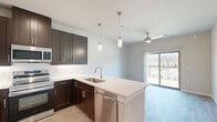 This thoughtfully designed one-bedroom, one-bathroom residence in Corinth, Texas offers a smart, efficient layout across a single floor. The open-concept living area seamlessly combines the kitchen, dining, and living spaces, creating a connected and functional environment. The kitchen is a standout feature, showcasing rich dark espresso cabinetry that extends to the ceiling for ample storage, bright white countertops, a peninsula with an undermount sink and pendant lighting overhead, and a full suite of stainless steel appliances including a refrigerator, range, microwave, and dishwasher. Light wood-look flooring runs throughout the main living areas, adding warmth and continuity. The living area is finished with a ceiling fan and opens directly to a private patio through a sliding glass door, inviting natural light and outdoor access. The bedroom offers plush carpeting, a ceiling fan, and a window with outdoor views, creating a comfortable and restful retreat. The bathroom features dark wood cabinetry, a white vanity countertop, and light wood-look flooring consistent with the rest of the home. Three closets provide generous storage throughout. Clean, neutral wall tones and modern finishes give the entire space a fresh, contemporary feel.