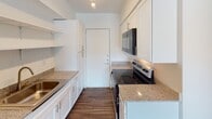 Located at 404 Kenniston Dr in Austin, TX, this single-story unit offers a practical and well-maintained layout with updated finishes throughout. The interior is unified by dark wood-style flooring that extends across the living, kitchen, and bedroom areas, providing a cohesive aesthetic.

The galley-style kitchen is efficiently designed, featuring granite-look countertops, white cabinetry with modern hardware, open wall shelving, and stainless steel appliances including a refrigerator, electric range, and over-the-range microwave. A single-basin sink and track lighting overhead complete the functional workspace. The kitchen opens directly toward the living area, creating a connected flow between the two spaces.

The living area is bright and open, receiving natural light through a front-facing window. A ceiling fan with a light fixture adds both comfort and practicality. A wall-mounted HVAC unit provides climate control. The bedroom continues the dark flooring and features soft sage-green walls, a ceiling fan, and a window with blinds that allows ample natural light.

The bathroom is clean and straightforward, finished in white with a shower/tub combination and chrome fixtures. Overall, the unit presents a tidy, move-in ready environment suited for everyday living in central Austin.