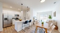 Located at 103 East Genesee Pointe Drive in West Henrietta, NY, this single-floor home offers three bedrooms and three bathrooms within a well-organized, efficiently designed layout. The open-concept living, dining, and kitchen area forms the heart of the home, creating a seamless flow between spaces. The kitchen is outfitted with white shaker-style cabinetry, stainless steel appliances including a range and over-the-range microwave, light quartz countertops, and a peninsula with bar seating illuminated by sleek pendant lighting. Light wood-look flooring runs throughout the main living areas, contributing to a clean, contemporary feel.

The living room receives abundant natural light through a large sliding glass door that opens to an outdoor view, enhancing the sense of openness. The adjacent dining area is defined by the same warm flooring and crisp white walls with panel-style doors featuring matte black hardware — a consistent design detail found throughout the home.

The three bedrooms feature neutral carpet and windows that bring in natural light. The bathrooms are finished in a clean, minimal style with wood-look flooring, white surrounds, and matte black fixtures. Two hallways connect the layout efficiently, keeping circulation clear throughout the single-floor footprint.