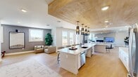 Located at 600–630 Martin Rd SW in Huntsville, Alabama, this single-floor space offers a thoughtfully designed open-concept layout that seamlessly integrates a kitchen, dining room, and living room into one cohesive environment. The interior is defined by a striking natural wood plank ceiling detail that anchors the kitchen zone, adding warmth and visual depth against the otherwise crisp white walls and light-toned luxury vinyl plank flooring found throughout.

The kitchen serves as the centerpiece of the space, featuring an expansive island with a ribbed panel base, white quartz countertop, and seating for multiple guests. A cluster of sleek black pendant lights hangs above the island, while stainless steel appliances and a bold geometric tile backsplash add contrast and character. White cabinetry lines the perimeter, maximizing storage and maintaining a clean aesthetic.

The dining area is situated adjacent to large windows that invite natural light and outdoor views, and is furnished with a round wood table beneath a modern pendant fixture. The living room features a contemporary tiled fireplace surround with an integrated media wall and a continuation of the wood ceiling detail, creating a warm yet modern retreat. A separate flex area with light blue walls and light wood flooring offers additional functional space within the layout.