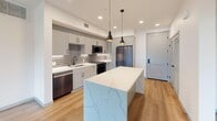 Located in Oxnard, CA, this well-designed 2-bedroom, 2-bathroom single-floor residence offers a thoughtful layout filled with contemporary finishes throughout. The open-concept kitchen serves as the heart of the home, anchored by a striking quartz waterfall island illuminated by modern pendant lights. Gray shaker cabinets, a subway tile backsplash, stainless steel appliances — including a gas range, built-in microwave, dishwasher, and refrigerator — and light hardwood-style flooring complete the polished look. The kitchen flows seamlessly into a bright living area with a ceiling fan and direct access to a private balcony, offering outdoor views of the surrounding landscape. Both bedrooms feature plush carpeting, ceiling fans, and windows that invite natural light. The generously sized primary bedroom includes a dedicated closet and an en-suite bathroom with marble-style tile flooring, a wide vanity with an LED-lit mirror, and matte black fixtures. The second bathroom features a tub-shower combo with crisp white tile surround and built-in shelving. Additional conveniences include a hallway, a second closet, and an in-unit laundry area, rounding out this modern and functional living space.