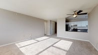 This single-floor residence is thoughtfully laid out to maximize both functionality and comfort. The open-concept living and dining area is finished with neutral-toned carpet and light gray walls, creating a clean, understated atmosphere. Natural light streams in through large windows and a sliding glass door that opens onto a private balcony, offering expansive outdoor views including distant hills and the surrounding cityscape. A ceiling fan overhead adds a practical touch to the living space.

The kitchen is positioned adjacent to the living area and is accessible via a breakfast bar with dark granite countertops. White shaker-style cabinetry lines the walls, complemented by stainless steel appliances including a refrigerator, gas range with overhead ventilation, and dishwasher. A window above the sink brings in additional natural light.

The bedroom is generously proportioned, carpeted, and features a wall-unit air conditioner, baseboard heating, and ample closet storage with sliding panel doors. The bathroom is cleanly finished in white, featuring subway tile walls, a full-size soaking tub with grab bar, a single vanity with under-cabinet storage, and a mirrored medicine cabinet.