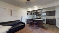 This single-floor residence offers a thoughtfully designed layout that balances function and comfort across its living, kitchen, bedroom, and bathroom spaces. The open-concept living area flows directly into the kitchen, anchored by a peninsula with granite-style countertops and bar seating for two — ideal for casual dining or entertaining. A ceiling fan overhead and plush carpeting underfoot lend the living space a relaxed, comfortable atmosphere.

The kitchen is a standout feature, finished with rich dark cabinetry, open display shelving, granite-style countertops, and wood-look flooring. It is fully equipped with a refrigerator, electric range, and microwave, with ample counter and storage space along both sides of the galley-style layout. A deep double-basin sink with a modern faucet adds practicality to the well-organized workspace.

Both bedrooms are generously sized, each featuring soft carpeting, ceiling fans, and textured ceilings. Natural light enters through large windows fitted with vertical blinds, creating a bright and airy feel. The bedrooms offer sufficient space for a full bedroom suite and additional furnishings.

The bathroom maintains the design consistency of the rest of the home, featuring a dark wood vanity with a granite-style countertop, a large mirror, wood-look tile flooring, and a well-lit vanity fixture above. The overall aesthetic throughout the space is cohesive, modern, and move-in ready.