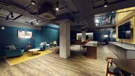 This two-floor entertainment venue blends industrial design with curated, lounge-style interiors across a generously scaled open layout. Exposed concrete columns, raw overhead ductwork, and dark painted ceilings define the industrial-chic character throughout, while warm wood-plank flooring and bold teal accent walls add a refined, welcoming contrast.

The main floor features distinct zones designed for socializing and relaxation. A bar counter with warm wood cabinetry, a back-lit pass-through window, and a row of terracotta-upholstered bar stools serves as a central gathering point. Adjacent to this is a comfortable lounge area with teal armchairs, a round coffee table, and a mustard area rug, ideal for casual conversation. Track lighting illuminates curated artwork displayed along the deep teal walls, adding visual interest throughout the open floor plan.

A dedicated media lounge occupies one corner, featuring a large flat-screen television mounted against richly patterned botanical wallpaper, complemented by layered rugs and plush seating. The entertainment offerings extend further with a collection of classic and modern arcade machines, including racing and retro cabinet games, positioned near the mezzanine level. An industrial-style railing defines the upper level transition, adding vertical dimension to the space. The overall ambiance is moody, energetic, and thoughtfully designed for entertainment and community gathering.