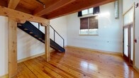 Located at 3500 Scotts Ln in Philadelphia's East Falls neighborhood, this two-floor loft space showcases a compelling blend of industrial and rustic design elements. Wide-plank pine hardwood floors run continuously throughout both levels, lending warmth and continuity to the open layout. Exposed timber beams and wood-plank ceilings on the lower floor contrast beautifully with the industrial-style exposed structural framing and ductwork visible on the upper level, creating a layered architectural aesthetic.

The main living area is generously proportioned, featuring track lighting mounted to the heavy timber framework, a built-in counter surface, and open sight lines that enhance the sense of volume. A sleek black metal staircase with pipe railings connects the two floors, anchored by a substantial wooden post that reinforces the space's raw, loft-like character. Natural light filters in through windows dressed with woven bamboo shades, adding to the warm, textured ambiance.

The kitchen is efficiently laid out with rich wood cabinetry, a tile backsplash, stainless steel appliances including a gas range and dishwasher, and exposed timber beams overhead. The bathroom features a soaking tub with a tile surround, a round vanity mirror, and a distinctive stone-textured accent wall. The upper floor offers an open secondary space with an exposed ceiling and access to natural light, well-suited for use as a studio, office, or sleeping area.