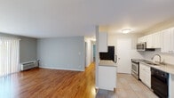This single-floor residence offers a functional and comfortable layout designed with everyday living in mind. The open-concept kitchen flows seamlessly into the living area, creating a connected and versatile space. The kitchen is equipped with white cabinetry, a stainless steel microwave and range, a black dishwasher, a double sink, and light stone-finish countertops. Large mirrored panels along the kitchen's partition wall enhance the sense of openness and reflect natural light throughout. Light tile flooring in the kitchen transitions to warm hardwood throughout the rest of the unit, lending a cohesive and inviting character to the space.

The living room is generously sized, featuring neutral gray walls, bright white trim, and a large sliding glass door dressed with vertical blinds that fills the space with natural light. Each bedroom continues the hardwood flooring and gray-toned walls, and each is served by a wall-mounted HVAC unit for individual climate control. The bedrooms offer windows with blinds and include open closets with built-in hanging rods for organized storage. The bathroom features a full-size soaking tub with a combination shower, framed by floor-to-ceiling neutral beige tile, offering a clean and practical finish throughout.