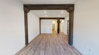 This single-floor space masterfully combines historic charm with modern upgrades, creating a compelling industrial-meets-contemporary aesthetic. The main living area makes an immediate impression with its striking dark wood post-and-beam framework, recessed lighting, and light-toned hardwood-style flooring that runs throughout the unit. A decorative barn-style sliding door adds a rustic, architectural touch.

Exposed red brick accent walls appear across multiple rooms, lending warmth and texture to the space. In the bedroom areas, arched brick window surrounds frame natural light beautifully, with ceiling fans providing added comfort. The brick detailing carries through to additional rooms, offering a consistent, character-rich atmosphere.

The kitchen is well-appointed with rich dark cabinetry, white countertops, and a full suite of stainless steel appliances including a refrigerator, range, microwave, and dishwasher. An adjacent utility area provides added convenience.

The bathroom features tile flooring, a clean white vanity with a large mirror, ample cabinetry, and a tiled shower. The layout flows efficiently, with thoughtful storage solutions including closets throughout.

Overall, this space offers a refined blend of preserved architectural heritage and updated modern living, creating an environment that is both distinctive and highly functional.