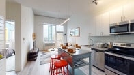 This well-designed single-floor unit offers a bright, contemporary living experience with a thoughtful open-concept layout. The kitchen is fully equipped with stainless steel appliances, including a refrigerator, electric range, microwave, and dishwasher, complemented by crisp white cabinetry, a subway tile backsplash, and a movable island with bar seating — ideal for casual dining and entertaining. Track lighting overhead enhances both function and style in this space.

The kitchen flows seamlessly into the living area, where large windows and a private balcony door flood the room with natural light and provide open urban skyline views. Light wood flooring runs throughout the main living space, contributing to the airy, modern ambiance.

The bedroom is a comfortable retreat featuring large windows that frame city views, soft carpet flooring, and a generously sized closet. The room is filled with natural light and maintains a calm, restful atmosphere.

The bathroom is finished with tile flooring and a modern vanity with ample counter space. A standout feature is the in-unit stacked washer and dryer, offering everyday convenience directly accessible from the bathroom. Throughout the unit, clean lines, neutral tones, and contemporary finishes create a cohesive, stylish living environment.