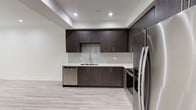 This contemporary single-floor space showcases a thoughtfully designed open layout with a cohesive modern aesthetic throughout. The kitchen is a standout feature, outfitted with dark wood-grain cabinetry extending from floor to ceiling, clean white quartz countertops, and a full suite of stainless steel appliances including a refrigerator, electric range, over-the-range microwave, and dishwasher. A subway tile backsplash adds a refined finishing touch, while recessed lighting illuminates the space effectively. Light-toned wood-look flooring runs consistently throughout the living and bedroom areas, complementing the neutral white walls and crisp white baseboards to create a bright, airy feel.

The bedroom benefits from a large window that invites natural light and frames a view of greenery outside. Recessed ceiling lights provide additional illumination, and a stepped ceiling detail adds architectural interest.

The bathroom is elegantly finished with large-format marble-look porcelain tile covering the floors and tub surround. A wide vanity with a white quartz countertop, undermount sink, and wood-grain cabinetry mirrors the kitchen's design language, while a glass-enclosed tub and shower combination completes the space with a polished, upscale feel.