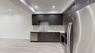 This contemporary single-floor space showcases a thoughtfully designed open layout with a cohesive modern aesthetic throughout. The kitchen is a standout feature, outfitted with dark wood-grain cabinetry extending from floor to ceiling, clean white quartz countertops, and a full suite of stainless steel appliances including a refrigerator, electric range, over-the-range microwave, and dishwasher. A subway tile backsplash adds a refined finishing touch, while recessed lighting illuminates the space effectively. Light-toned wood-look flooring runs consistently throughout the living and bedroom areas, complementing the neutral white walls and crisp white baseboards to create a bright, airy feel.

The bedroom benefits from a large window that invites natural light and frames a view of greenery outside. Recessed ceiling lights provide additional illumination, and a stepped ceiling detail adds architectural interest.

The bathroom is elegantly finished with large-format marble-look porcelain tile covering the floors and tub surround. A wide vanity with a white quartz countertop, undermount sink, and wood-grain cabinetry mirrors the kitchen's design language, while a glass-enclosed tub and shower combination completes the space with a polished, upscale feel.