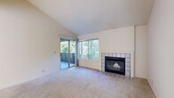 This single-story residence in Driftwood, California offers a thoughtfully laid-out floor plan with two bedrooms and two bathrooms. The living room serves as the centerpiece of the home, distinguished by soaring vaulted ceilings that lend an open, airy quality to the space. A tile-surround fireplace anchors one wall, providing a classic focal point, while a large picture window and sliding glass door flood the room with natural light and frame views of surrounding mature trees. The sliding door opens directly onto a private balcony, extending the living space outdoors.

The kitchen features white cabinetry, dark countertops, a double stainless steel sink, and a window that brings in additional natural light. Both bedrooms are carpeted and well-proportioned, with one bedroom offering its own sliding glass door and balcony access overlooking the wooded scenery. The bathrooms are clean and functional, each featuring a tub-shower combination, wood-look flooring, and a window for ventilation. Neutral tones and plush carpeting throughout the main living areas contribute to a calm, cohesive ambiance across the entire home.