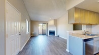 Located at 2130 S Santa Fe Ave in Vista, CA, this one-bedroom, one-bathroom residence offers a thoughtfully designed layout across a single floor. The open-concept living and dining area impresses with vaulted ceilings, a ceiling fan, and light-toned wood-look flooring that extends throughout the space. A corner fireplace serves as a focal point, while a sliding glass door opens to a private balcony with tree-lined views of the surrounding neighborhood. The kitchen features gray-toned cabinetry, granite-style countertops, stainless steel appliances including a gas range and dishwasher, and a skylight that fills the space with natural light. A pass-through opening connects the kitchen to the living area for an open feel. The spacious bedroom offers a large window with natural views and access to a generous walk-in closet with built-in shelving and hanging rods. The full bathroom includes a white vanity with ample counter space, a large mirror, and a tub-shower combination. Neutral beige tones, white trim, and textured ceilings provide a clean, cohesive aesthetic throughout the residence.