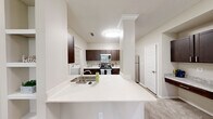 Located at 2158 Cumberland Pkwy SE in Atlanta, GA, this well-appointed one-bedroom, one-bathroom residence offers a thoughtfully designed single-floor layout. The living room features vaulted ceilings, soft carpeting, a classic white-mantled fireplace, and built-in shelving, creating a warm and functional gathering space. Adjacent to the living area, the dining room is highlighted by crown molding, a stylish pendant light, and a sliding glass door that opens to a private patio with lush outdoor views. The kitchen is outfitted with rich dark cabinetry, a subway tile backsplash, stainless steel appliances, and an expansive quartz peninsula countertop with an integrated sink — ideal for both cooking and casual dining. A dedicated desk nook with matching cabinetry and granite countertop adds a practical workspace. The bedroom is a comfortable retreat with plush carpeting, natural light from a large window, and a ceiling fan. A spacious walk-in closet with wire shelving provides ample storage. The bathroom features wood-look flooring, a granite-topped vanity, and a full tub-shower combination. Completing the layout, an in-unit laundry room accommodates a full-size washer and dryer with overhead shelving.