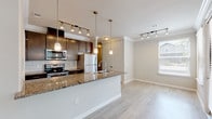 This single-floor, one-bedroom, one-bathroom residence offers a thoughtfully designed layout that maximizes functionality and comfort. The open-concept kitchen serves as the centerpiece of the living space, anchored by a large peninsula with granite countertops and an integrated sink. Dark espresso cabinetry provides generous storage and pairs with a classic subway tile backsplash for a clean, modern aesthetic. Stainless steel appliances, including a refrigerator, range, and microwave, complete the kitchen. Pendant lighting and a track light system illuminate both the kitchen and the adjacent living area, which benefits from natural light provided by a window with blinds. Crown molding runs throughout, adding a refined architectural detail to every room. Light wood-style flooring extends seamlessly across the living areas and bedroom, creating a cohesive and easy-to-maintain surface. The bedroom is a calm, neutral space with its own window and ample room for furnishings. The bathroom features a granite-topped vanity with dark cabinetry, a soaking tub, and large-format tile surrounding the tub and shower, completing the consistent design language found throughout the unit.
