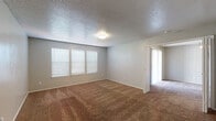 This single-floor residence offers a straightforward and functional layout designed for comfortable everyday living. The living area greets you upon entry through a solid white front door, featuring warm brown carpeting, neutral gray walls, and a flush-mount ceiling light. A window with horizontal blinds allows natural light to fill the space. The adjoining room serves as a spacious primary bedroom, complete with plush carpeting, a ceiling fan with light kit, and large vertical blinds covering a broad window — ideal for light control and privacy.

A secondary carpeted bedroom also benefits from natural light through double windows with blinds, offering a versatile space for sleeping or use as a home office. The kitchen is efficiently arranged in a galley style, featuring gray cabinetry, speckled laminate countertops, a double stainless steel sink, and black appliances including a refrigerator, range, and dishwasher. Light wood-look flooring runs through the kitchen, adding a clean contrast to the cabinetry.

The bathroom is well-equipped with a single-basin vanity set in a speckled countertop, gray under-sink cabinetry, a large mirror, and a combined tub and shower with white tile surround. Wood-look flooring continues here, tying together the wet areas of the home. Throughout, textured ceilings and consistent neutral tones create a cohesive, move-in-ready environment.
