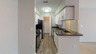This single-floor residence offers a well-organized layout designed for comfortable everyday living. The galley-style kitchen is efficiently arranged with white shaker cabinetry, dark granite-style countertops, a stainless steel sink, and stainless steel appliances including a refrigerator and range. Wood-look luxury vinyl plank flooring runs throughout the kitchen, lending warmth and easy maintenance to the space. A dedicated laundry closet with louvered doors is conveniently accessible from the kitchen corridor. The two bedrooms are generously proportioned, each featuring soft wall-to-wall carpeting in neutral tones, white horizontal blinds providing natural light control, and clean white trim throughout. One bedroom includes a walk-in closet, offering ample storage. Both full bathrooms are finished with wood-look vinyl flooring, white tub/shower surrounds, brushed nickel fixtures and towel bars, and white vanities, providing a cohesive and tidy aesthetic. The overall color palette throughout the residence is neutral and understated, with soft gray walls creating a calm, move-in-ready environment. A ceiling fan is present in the main living area, adding both function and airflow. The thoughtful floor plan connects all spaces in a practical and intuitive manner.