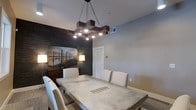 Located at 2170 Benton Blvd in Savannah, Georgia, this single-story residence offers a thoughtfully designed interior with modern finishes and contemporary styling. The dining area serves as a standout space, anchored by a striking geometric wood chandelier that draws the eye upward and casts warm, focused light over a substantial concrete-top dining table surrounded by upholstered cream chairs. A bold dark stone accent wall adds dramatic contrast to the otherwise neutral, light gray palette of the walls, creating a sophisticated backdrop for the space. Decorative artwork and warm accent lighting from coordinating floor lamps further enhance the ambiance, contributing to a refined yet welcoming atmosphere. The clean white trim and doors provide crisp definition throughout, while the light-toned flooring adds continuity and a sense of openness across the single level. The overall design blends industrial and contemporary elements seamlessly, resulting in a space that feels both stylish and functional. This Savannah property combines modern interior design sensibilities with a cohesive aesthetic that makes it a distinctive and well-appointed home.
