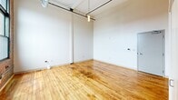 Located at 95 Chestnut St in the heart of Providence, RI, this loft-style unit delivers an impressive blend of industrial character and functional design across a single floor. The main living area immediately captures attention with its soaring ceiling height, warm honey-toned hardwood floors, and crisp white walls. Exposed overhead ductwork and pendant lighting reinforce the industrial aesthetic, while the open layout maximizes the sense of space.

The kitchen runs along one wall in a galley configuration, outfitted with white shaker cabinetry, stainless steel appliances including a range and refrigerator, and a granite-style countertop with an integrated sink. Large black-framed windows flood the kitchen with natural light and offer views of the surrounding Providence streetscape, while an exposed brick wall adds raw, historic texture to the space.

The bathroom is clean and well-appointed, featuring light tile flooring, a white vanity with an undermount sink and stone countertop, a framed mirror, and a tiled shower area. Its neutral palette provides a calm contrast to the loft's industrial character.

Overall, this unit at 95 Chestnut St offers a distinctive urban living experience, combining the architectural heritage of a classic Providence building with updated finishes and modern conveniences.