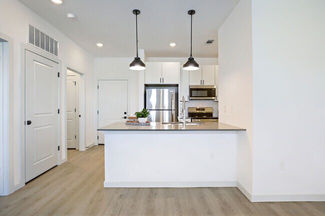El modelo BH-A1 (L) incluye una cocina totalmente equipada con gabinetes blancos estilo shaker, salpicadero de azulejos en espiga, electrodomésticos de acero inoxidable y elegantes lámparas colgantes. Garrett Harvest Junction West, Longmont, CO. - Garrett Harvest Junction West