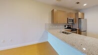 This single-floor unit offers a thoughtfully designed open-concept layout that seamlessly connects the kitchen and living area, creating a bright and functional living space. Light wood-tone flooring flows throughout, complementing the neutral walls and recessed lighting that illuminate the interior.

The kitchen is a standout feature, equipped with stainless steel appliances including a gas range, built-in microwave, dishwasher, and refrigerator. Light wood cabinetry with sleek hardware provides ample storage, while granite-style countertops and a tile backsplash lend a clean, contemporary aesthetic. A peninsula counter with a sink extends into the living area, enhancing the open flow and offering additional workspace.

The living area is generously proportioned, bathed in natural light from a large window that frames outdoor views. The open layout provides flexible arrangements for furnishing and everyday use.

The bathroom is finished in crisp white tones with light tile flooring and features a full bathtub with shower, grab bars for added accessibility, and clean, minimal fixtures throughout.

Overall, this unit delivers a modern and functional design with quality finishes, an abundance of natural light, and a cohesive aesthetic that makes it both practical and inviting.