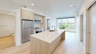 Located at 333 SE 120th Ave in Vancouver, WA, this thoughtfully designed 2-bedroom, 2-bathroom unit offers a clean, modern aesthetic throughout its single-floor layout. The open-concept kitchen serves as the heart of the home, featuring light wood cabinetry, a large center island with a white quartz countertop and undermount sink, and a full suite of stainless steel appliances including a refrigerator, range, and microwave. Light hardwood-style flooring runs through the main living and kitchen areas, complementing the bright, neutral palette and recessed lighting overhead. A large floor-to-ceiling window in the living area fills the space with natural light and offers open outdoor views of the surrounding landscape. The spacious primary bedroom includes plush carpeting, a walk-in closet, and direct access to an en-suite bathroom. The second bedroom also features carpeted floors, a wall-mounted HVAC unit, and a window with pleasant outdoor views. Both bathrooms are finished in crisp white, with one featuring a full soaking tub and shower combination. A hallway bathroom conveniently incorporates a stacked washer and dryer unit alongside light hardwood-style flooring, adding practical functionality to the overall layout.