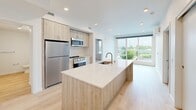 Located at 333 SE 120th Ave in Vancouver, WA, this thoughtfully designed 2-bedroom, 2-bathroom unit offers a clean, modern aesthetic throughout its single-floor layout. The open-concept kitchen serves as the heart of the home, featuring light wood cabinetry, a large center island with a white quartz countertop and undermount sink, and a full suite of stainless steel appliances including a refrigerator, range, and microwave. Light hardwood-style flooring runs through the main living and kitchen areas, complementing the bright, neutral palette and recessed lighting overhead. A large floor-to-ceiling window in the living area fills the space with natural light and offers open outdoor views of the surrounding landscape. The spacious primary bedroom includes plush carpeting, a walk-in closet, and direct access to an en-suite bathroom. The second bedroom also features carpeted floors, a wall-mounted HVAC unit, and a window with pleasant outdoor views. Both bathrooms are finished in crisp white, with one featuring a full soaking tub and shower combination. A hallway bathroom conveniently incorporates a stacked washer and dryer unit alongside light hardwood-style flooring, adding practical functionality to the overall layout.