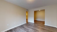This single-floor residence offers a clean, modern aesthetic across all of its rooms, unified by warm neutral wall tones and durable hardwood-style flooring that runs throughout the living areas and bedrooms. The open living area greets residents with a sliding glass door that invites natural light and provides access to an outdoor balcony, creating a bright and airy atmosphere. The layout connects seamlessly to additional rooms, including a dedicated dining or secondary living space visible through an open passageway.

The kitchen is thoughtfully designed with an abundance of white shaker-style cabinetry, light-toned countertops, and white appliances including an electric range and refrigerator. A double basin sink sits beneath upper cabinets, maximizing both storage and functionality in a well-organized galley-style layout.

The bedrooms are generously sized, each featuring the same warm flooring and neutral walls, offering a versatile canvas for a variety of furnishing arrangements. Ceiling vents provide consistent climate control throughout.

The bathroom is a standout feature, finished with striking marble-style tile covering both the floor and the full tub surround. The soaking tub with chrome fixtures adds a refined touch, while the overall design maintains a clean, contemporary feel throughout the space.
