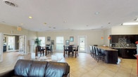 This single-floor communal space is thoughtfully designed to accommodate both relaxed gatherings and more structured social settings. The layout is divided into several functional zones, each with its own distinct character while contributing to a cohesive overall ambiance.

The main lounge area features soaring ceilings that lend an open, airy feel to the space. Elegant cream-toned sofas and wingback chairs are arranged around a striking floor-to-ceiling stone fireplace, which serves as the room's focal point. A rustic wooden mantel tops the fireplace, accented by decorative accessories. Black-trimmed French doors flank the fireplace, allowing abundant natural light to flood the interior and providing views of the exterior.

Modern drum chandeliers and recessed lighting provide layered illumination throughout. The lounge transitions seamlessly into additional seating areas outfitted with plush sofas, accent chairs, and side tables, creating intimate conversation spaces.

The dining area features multiple dark wood pub-height tables paired with upholstered chairs, arranged to accommodate groups of varying sizes. Light tile flooring, neutral wall tones, and framed artwork contribute to the welcoming atmosphere. Together, these spaces offer a versatile, well-appointed environment suited for a variety of communal activities.