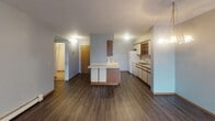 Located at 725 42nd St S in Fargo, North Dakota, this single-floor unit offers a practical and functional layout across several well-defined living spaces. The open living and dining area is finished with dark hardwood-style flooring and features a chandelier light fixture, a wall-mounted air conditioning unit, and a large sliding glass door framed by vertical blinds that draws in natural light. The textured ceiling adds a classic touch throughout the main living spaces. The kitchen is designed for efficiency, featuring a central island with a built-in cooktop, white cabinetry with wood-trimmed accents, open shelving, and a full suite of white appliances including a refrigerator, dishwasher, and electric range. A stainless steel sink with a window view completes the functional workspace. The bedroom is finished with plush carpeting, soft blue-gray walls, a textured ceiling, and a window with vertical blinds that allows ample natural light, along with a baseboard heating unit. The bathroom is clean and well-appointed, featuring tile flooring, a single-sink vanity with a large mirror, and a full tub-shower combination. The overall ambiance is simple, neutral, and move-in ready, offering comfortable everyday living in a quiet Fargo neighborhood.