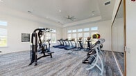 Located at 2500 Peaceful River Dr in Mount Dora, FL, this well-appointed fitness center offers a comprehensive workout facility across a single, generously sized floor. The space is divided into two distinct areas: a main gym floor and a separate yoga/movement studio.

The main gym is bright and open, characterized by elevated tray ceilings, recessed lighting, and large ceiling fans that promote airflow throughout the space. Rows of floor-to-ceiling windows line the walls, flooding the interior with natural light and offering views of the surrounding greenery and outdoor pool area. The gym is outfitted with an extensive selection of equipment, including multiple treadmills, elliptical machines, rowing machines, stationary bikes, cable machines, strength training stations, and a full dumbbell rack. A large framed mirror enhances the sense of space. The floor is finished with durable, patterned carpet.

The adjoining yoga and movement studio features a clean, minimalist design with light hardwood-style flooring, floor-to-ceiling mirrors, and expansive windows that bring in abundant natural light and outdoor views. The studio provides an ideal setting for stretching, yoga, and low-impact training. Together, both areas create a well-rounded, modern fitness facility suited for a wide range of workout routines.