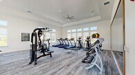 Located at 2500 Peaceful River Dr in Mount Dora, FL, this well-appointed fitness center offers a comprehensive workout facility across a single, generously sized floor. The space is divided into two distinct areas: a main gym floor and a separate yoga/movement studio.

The main gym is bright and open, characterized by elevated tray ceilings, recessed lighting, and large ceiling fans that promote airflow throughout the space. Rows of floor-to-ceiling windows line the walls, flooding the interior with natural light and offering views of the surrounding greenery and outdoor pool area. The gym is outfitted with an extensive selection of equipment, including multiple treadmills, elliptical machines, rowing machines, stationary bikes, cable machines, strength training stations, and a full dumbbell rack. A large framed mirror enhances the sense of space. The floor is finished with durable, patterned carpet.

The adjoining yoga and movement studio features a clean, minimalist design with light hardwood-style flooring, floor-to-ceiling mirrors, and expansive windows that bring in abundant natural light and outdoor views. The studio provides an ideal setting for stretching, yoga, and low-impact training. Together, both areas create a well-rounded, modern fitness facility suited for a wide range of workout routines.