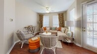 This single-floor residence offers a thoughtfully designed layout that balances comfort and functionality across its key living areas. The living room serves as the heart of the home, featuring rich hardwood flooring, a ceiling fan with light fixture, and multiple windows dressed with classic white blinds and vibrant floral curtains that fill the space with natural light. A sectional sofa and eclectic seating arrange naturally around a central coffee table, creating an inviting atmosphere.

The open-concept layout transitions seamlessly into the dining area, which benefits from large windows and recessed lighting, and connects directly to the kitchen via a peninsula breakfast bar with seating for two. The kitchen is equipped with warm wood cabinetry, granite-style countertops, and black appliances including a range, over-the-range microwave, and refrigerator, alongside an in-unit laundry area.

The primary bedroom features plush carpet, a ceiling fan, a natural-light window with blinds, and generous wall space ideal for artwork. A second bedroom offers carpeted flooring, a walk-in closet, and direct access to the full bathroom. The bathroom is outfitted with a tub-shower combination, wood cabinetry with overhead storage, and hardwood flooring, completing this well-rounded and functional living space.