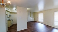 This single-story unit is organized into a functional and practical layout, with distinct living, kitchen, sleeping, and bathroom areas. The open living and dining area is finished with dark hardwood-style flooring that runs throughout the main living spaces, creating a cohesive look. A decorative chandelier accents the dining area, while natural light enters through a window fitted with horizontal blinds near the front entry door. A standout feature of the living area is the built-in shelving and cabinetry unit along one wall, offering ample display and storage space.

The galley-style kitchen is efficiently arranged with white cabinetry on both sides, granite-style countertops, a double stainless steel sink, and a white electric range with overhead ventilation. Upper cabinets maximize vertical storage throughout the kitchen.

Two bedrooms are finished with plush carpet and each include a window with blinds, allowing natural light while maintaining privacy. The rooms offer generous wall space suitable for a variety of furniture arrangements.

The bathroom includes a full tub and shower combination with a chrome fixtures, overhead cabinetry for storage, a toilet, and a vanity with sink. Dark hardwood-style flooring extends into the bathroom, tying the space together cohesively.