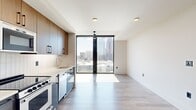 Located in the heart of Midtown Atlanta at 1382 Peachtree St NE, this modern studio offers a thoughtfully designed open-concept layout combining the kitchen and living area into one cohesive space. The unit is anchored by dramatic floor-to-ceiling windows framed in sleek black, flooding the interior with abundant natural light and delivering sweeping views of the Atlanta skyline and surrounding cityscape. Light-toned hardwood-style flooring runs throughout, complementing the clean white walls and contemporary aesthetic.

The kitchen is well-appointed with a full suite of stainless steel appliances, including a refrigerator, gas range, built-in microwave, and dishwasher. Two-toned cabinetry — warm wood upper cabinets paired with matte slate-blue lower cabinets — adds visual depth, while a white tile backsplash and light countertops complete the modern look. A stacked in-unit washer and dryer are conveniently tucked behind a dedicated closet door.

The bathroom features large-format beige tile flooring, a glass-enclosed walk-in shower with full-height dark tile surround, a wall-mounted illuminated mirror, and a floating wood vanity with an undermount sink. A ceiling fan in the living area and recessed lighting throughout round out this polished, functional space.