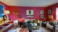 Located at 5400 Beverly Hills Dr in Columbus, Ohio, this single-floor residence makes an immediate impression with its vivid and eclectic interior design. The living area serves as the heart of the home, showcasing bold crimson-red accent walls that create a dramatic and energetic atmosphere. Carefully curated artwork adorns the walls, including a striking black-and-white graphic print as a focal centerpiece, complemented by framed zebra-print artwork that adds a sophisticated, wildlife-inspired aesthetic. A decorative metallic wall medallion further enhances the artistic character of the space. The room is furnished with a cream-toned sofa dressed in an array of patterned throw pillows, paired with a zebra-print accent chair that reinforces the space's bold design theme. A tall Asian-inspired lantern lamp provides warm, ambient lighting alongside a sleek brass table lamp. Lush tropical greenery in the form of a potted palm plant introduces a natural element, softening the room's vibrant palette. The flooring is carpeted, adding warmth and comfort underfoot. Overall, the space exudes a confident, globally inspired personality, blending bold color, eclectic art, and layered textures into a cohesive and visually dynamic living environment.