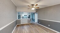This single-floor residence offers a thoughtfully designed layout with a cohesive aesthetic throughout. The living area is finished with light wood-look flooring and features a two-tone gray wall treatment accented by white chair-rail molding, creating a clean and modern look. A ceiling fan with integrated lighting anchors the room, while a built-in shelving unit with a pass-through window connects the living space directly to the kitchen, enhancing the open feel of the floor plan.

The kitchen is well-equipped with white shaker-style cabinetry, dark granite-look countertops, and a full suite of stainless steel appliances including a refrigerator, electric range, and over-the-range microwave. A skylight above the kitchen fills the space with natural light, and the wood-look flooring carries through seamlessly from the main living area.

The bedroom is carpeted for comfort and features the same two-tone gray wall treatment, a ceiling fan, and a window that brings in natural light. The full bathroom includes a single-sink vanity with under-sink storage and a tub-shower combination.

A dedicated laundry room provides added convenience with an in-unit washer and dryer, along with a water heater, keeping all utilities centrally located within the home.