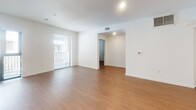 Located on Wilshire Boulevard in the heart of Los Angeles, this single-floor, 3-bedroom, 2-bathroom unit offers a clean, modern aesthetic throughout. The open-concept kitchen and living area serves as the central hub of the space, featuring white high-gloss cabinetry, a full suite of stainless steel appliances including a refrigerator, dishwasher, microwave, and range, and warm wood-tone laminate flooring that extends throughout the unit. Recessed lighting illuminates the kitchen, while the adjacent living area benefits from generous natural light through large windows and a glass door that opens to a balcony. The bedrooms are bright and simply appointed, each with white walls, wood-tone flooring, and windows fitted with blinds. The primary bedroom is a comfortable, private retreat. A dedicated walk-in closet features built-in shelving and a hanging rod, providing well-organized storage. Both bathrooms are finished with wood-look tile flooring, tub-shower combinations clad in large-format stone-effect tile, and vanities with warm wood cabinetry and light countertops. A hallway connects all rooms efficiently, contributing to a functional and cohesive floor plan throughout the unit.