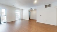 Located on Wilshire Boulevard in the heart of Los Angeles, this single-floor, 3-bedroom, 2-bathroom unit offers a clean, modern aesthetic throughout. The open-concept kitchen and living area serves as the central hub of the space, featuring white high-gloss cabinetry, a full suite of stainless steel appliances including a refrigerator, dishwasher, microwave, and range, and warm wood-tone laminate flooring that extends throughout the unit. Recessed lighting illuminates the kitchen, while the adjacent living area benefits from generous natural light through large windows and a glass door that opens to a balcony. The bedrooms are bright and simply appointed, each with white walls, wood-tone flooring, and windows fitted with blinds. The primary bedroom is a comfortable, private retreat. A dedicated walk-in closet features built-in shelving and a hanging rod, providing well-organized storage. Both bathrooms are finished with wood-look tile flooring, tub-shower combinations clad in large-format stone-effect tile, and vanities with warm wood cabinetry and light countertops. A hallway connects all rooms efficiently, contributing to a functional and cohesive floor plan throughout the unit.
