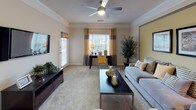 This single-floor residence offers a thoughtfully designed layout that balances comfort and functionality throughout. The living room serves as the heart of the home, featuring plush carpeting, crown molding, a ceiling fan, and a distinctive gold accent wall framed in gray, creating a warm and inviting focal point. Natural light streams in through large windows dressed with two-tone curtains, while ample space accommodates both a seating area and a dedicated workspace. Adjacent to the living room, the dining area showcases rich wood-look flooring, a tray ceiling with recessed lighting, and seamless access to both the kitchen and bathroom. The galley-style kitchen is equipped with white cabinetry, dark countertops, wood-look flooring, and black appliances including a refrigerator and electric range. The two bedrooms each offer carpeted floors, generous natural light from multiple windows, and a calm, restful ambiance — one featuring a cool blue accent wall. Both bathrooms are finished with wood-look flooring, vanities with ample storage, and tub-shower combinations. Completing the home is a dedicated in-unit laundry room with a full-size washer and dryer and overhead shelving for added storage convenience.