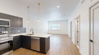 Located on Germantown Avenue in Philadelphia's historic Germantown neighborhood, this thoughtfully designed one-bedroom, one-bathroom unit offers a modern living experience with quality finishes throughout. The open-concept layout connects the kitchen and living area, creating a bright, airy feel enhanced by recessed lighting and natural light from large windows. Warm-toned hardwood-style flooring runs throughout the space, adding cohesion and warmth.

The kitchen is a standout feature, centered around a large island with a white quartz countertop, undermount sink, and stylish brass pendant lighting. Dark, flat-front cabinetry pairs with a blue-gray subway tile backsplash, while stainless steel appliances — including a refrigerator, range, microwave, and dishwasher — complete the modern aesthetic.

The bedroom is a comfortable, well-proportioned retreat with a large window overlooking the surrounding area and two dedicated closets with paneled doors and matte black hardware. The full bathroom features a soaking tub with a striking floor-to-ceiling vertical blue tile surround and matte black fixtures. A dedicated laundry area adds everyday convenience, rounding out this well-appointed urban residence.