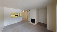 This single-floor residential unit offers a practical and comfortable layout designed for everyday living. The living room serves as the heart of the space, featuring plush carpeting, a textured ceiling, a wood-burning fireplace flanked by built-in shelving, and a ceiling fan. A pass-through counter connects the living area to the galley-style kitchen, which is equipped with wood-toned cabinetry, laminate countertops, a double-basin sink, a coil electric range, and a full-size refrigerator — all finished in white. Durable vinyl flooring runs throughout the kitchen. The bedrooms are carpeted and finished with neutral walls, textured ceilings, and window blinds that allow for natural light. One bedroom features a sliding glass door that opens to a private balcony, providing a pleasant outdoor retreat. The full bathroom includes a single-sink vanity with wood cabinetry, a large wall mirror with overhead lighting, a combined shower and soaking tub with white tile surround, and patterned vinyl flooring. Throughout the unit, the warm, neutral color palette and consistent finishes create a cohesive and functional living environment.